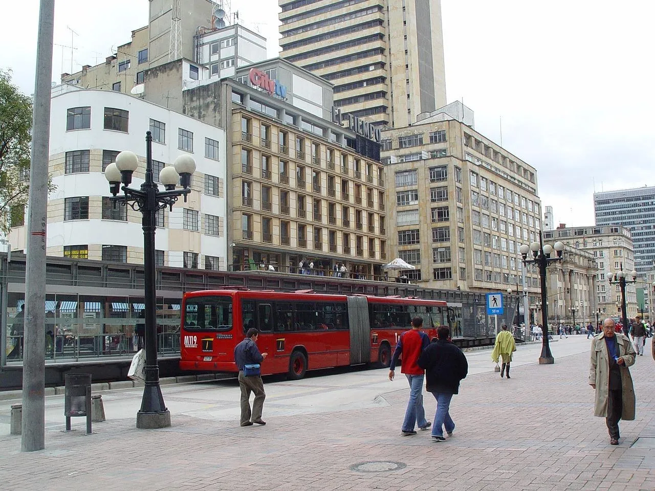 Un bus articulado rojo en una estación de carril exclusivo en una calle de la ciudad
